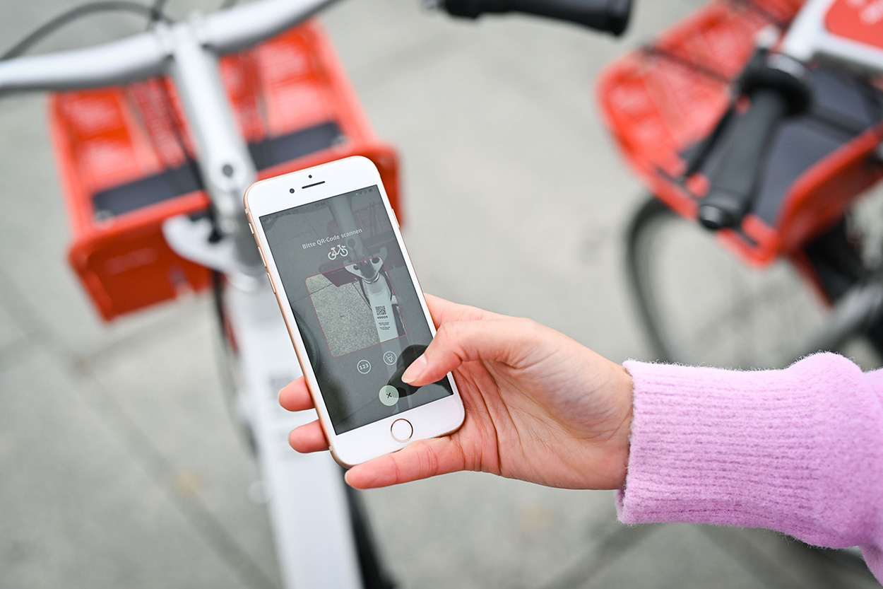 Eine Hand hält ein Smartphone, im Hintergrund sind Räder zu sehen