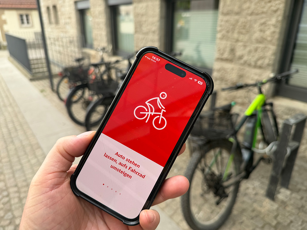 Ein Handy, auf dem eine App zu sehen ist, im Hintergrund Fahrräder